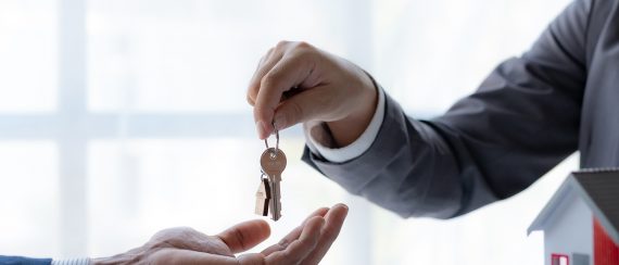 Real estate agent giving house key to the client after signing the real estate contract. Home and real estate trading concept.