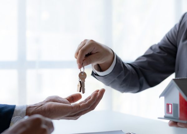 Real estate agent giving house key to the client after signing the real estate contract. Home and real estate trading concept.