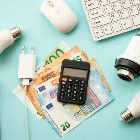 Utility payments. Electricity and heating savings concept. Led lamp, thermostat, calculator, keyboard and electric cable at blue. Top view.