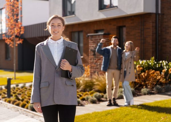 Smiling real estate agent standing outdoors while happy couple celebrates buying new house