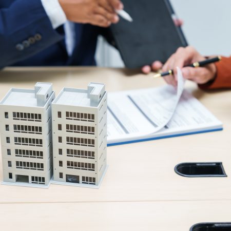 A businessman desk in a sales office sells a condo building customer.They agree to sign a contract