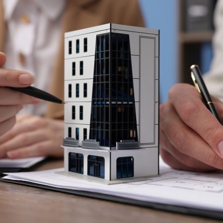Real estate agent working with client at desk with house model in office, closeup